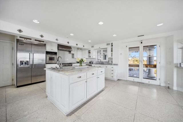 kitchen featuring wall chimney exhaust hood, white cabinetry, appliances with stainless steel finishes, a kitchen island, and light stone countertops