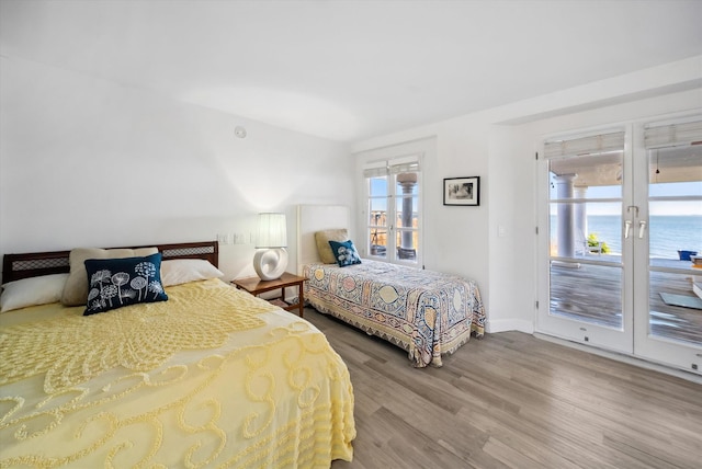 bedroom featuring access to exterior, hardwood / wood-style floors, french doors, and a water view