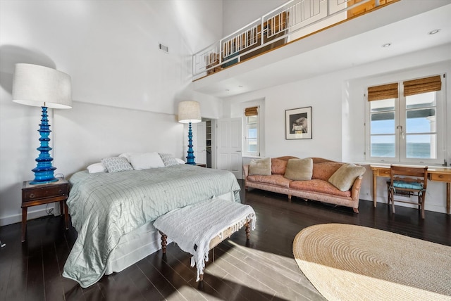 bedroom with dark hardwood / wood-style flooring, a towering ceiling, and multiple windows