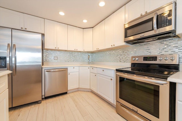 kitchen with sink, appliances with stainless steel finishes, backsplash, white cabinets, and light wood-type flooring