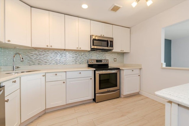 kitchen with appliances with stainless steel finishes, sink, white cabinets, and decorative backsplash