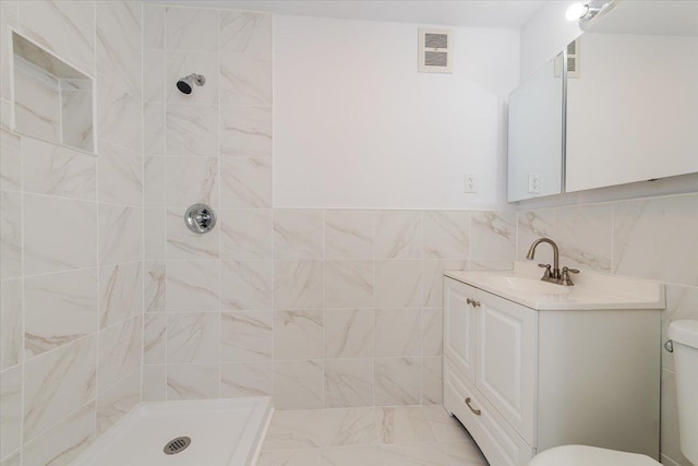 bathroom with vanity, a tile shower, tile walls, and toilet