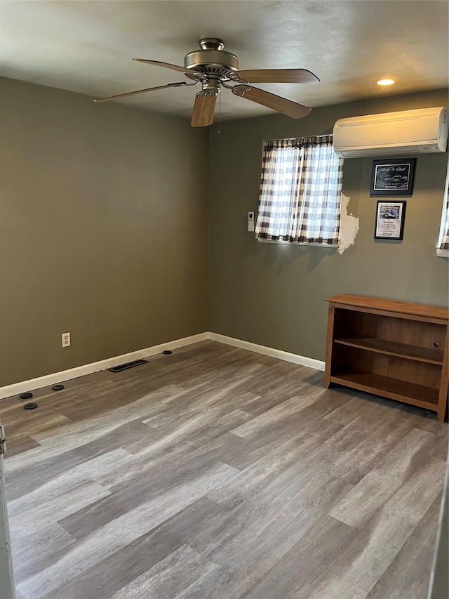 unfurnished room featuring ceiling fan, a wall mounted air conditioner, and light hardwood / wood-style flooring