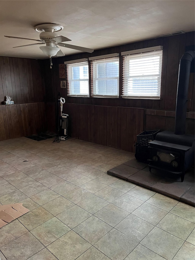 interior space featuring ceiling fan, wooden walls, and a wood stove