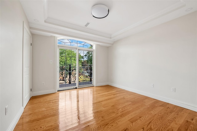 empty room with a raised ceiling, ornamental molding, and light hardwood / wood-style floors