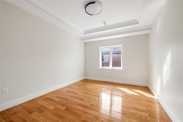 empty room featuring ornamental molding, a raised ceiling, and light hardwood / wood-style flooring