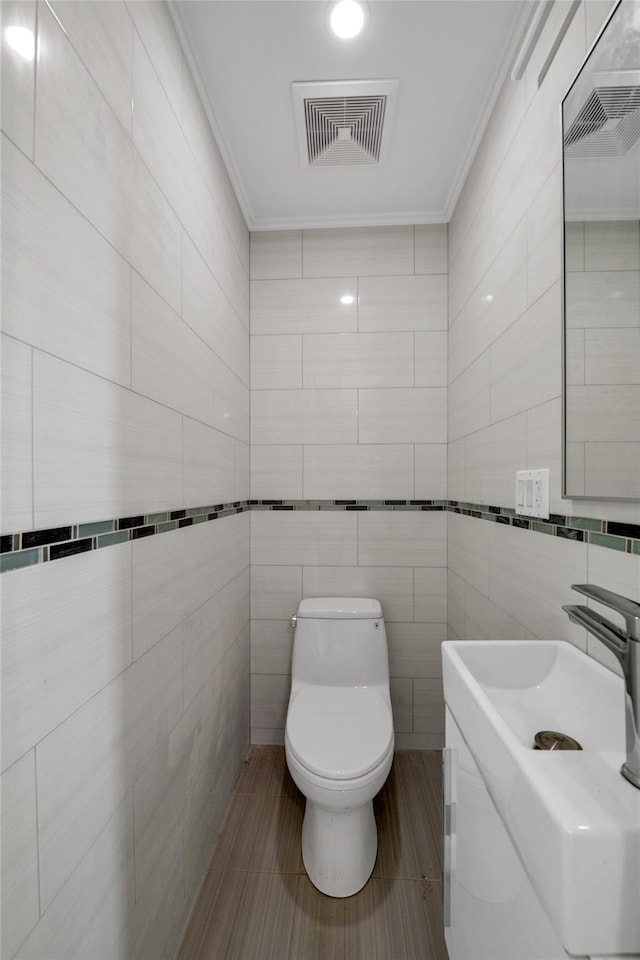 bathroom with tile walls, vanity, crown molding, and toilet