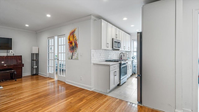 kitchen with appliances with stainless steel finishes, tasteful backsplash, ornamental molding, white cabinets, and light wood-type flooring