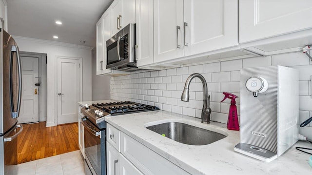 kitchen with sink, light stone counters, ornamental molding, appliances with stainless steel finishes, and white cabinets