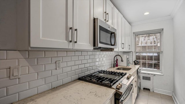 kitchen with radiator, white cabinetry, sink, stainless steel appliances, and light stone countertops