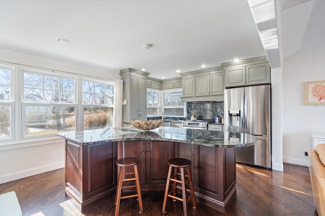 kitchen featuring stainless steel appliances, dark stone countertops, a kitchen bar, and decorative backsplash