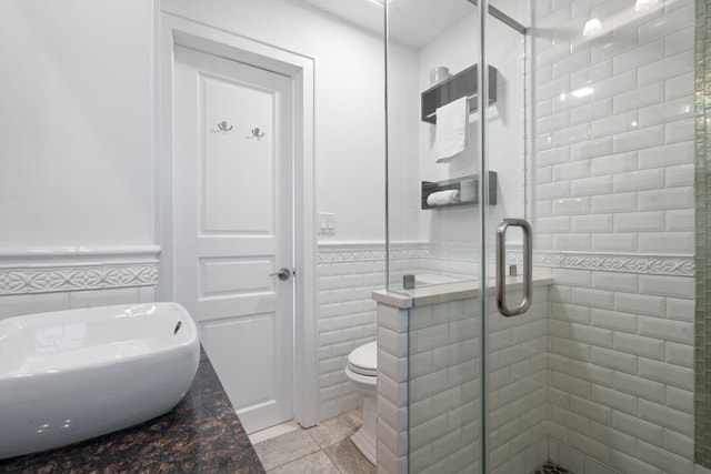 bathroom featuring tile patterned floors, toilet, a shower with shower door, and tile walls