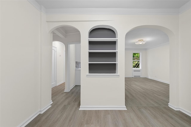 spare room with crown molding, built in shelves, and light hardwood / wood-style flooring