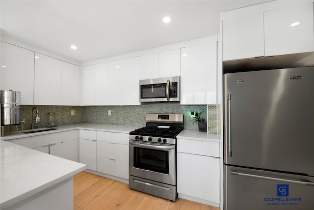 kitchen featuring sink, light hardwood / wood-style flooring, appliances with stainless steel finishes, white cabinets, and decorative backsplash