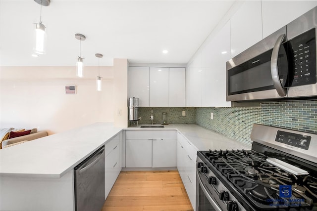 kitchen with decorative light fixtures, kitchen peninsula, white cabinets, and appliances with stainless steel finishes