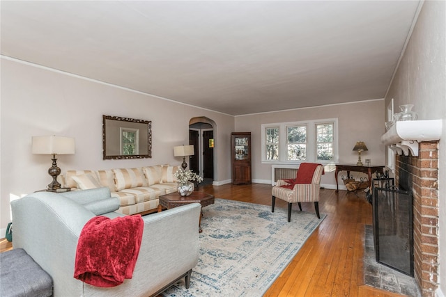 living room with crown molding, a brick fireplace, hardwood / wood-style flooring, and radiator heating unit