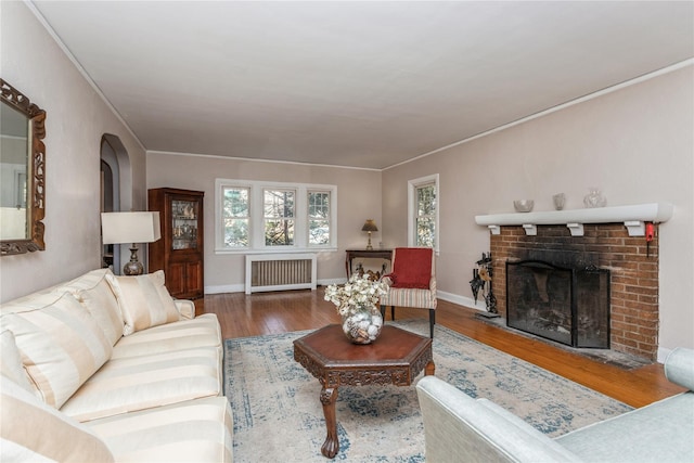 living room featuring a healthy amount of sunlight, a brick fireplace, radiator, and hardwood / wood-style floors