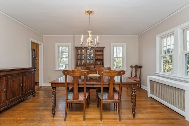 dining space with ornamental molding, radiator heating unit, light hardwood / wood-style flooring, and a notable chandelier