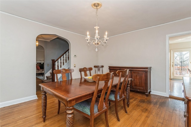 dining area with wood-type flooring, ornamental molding, and a chandelier