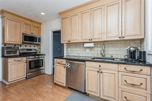 kitchen featuring sink, stainless steel appliances, light hardwood / wood-style floors, decorative backsplash, and dark stone counters