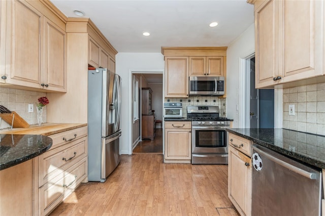 kitchen featuring appliances with stainless steel finishes, light brown cabinetry, light hardwood / wood-style floors, and dark stone countertops