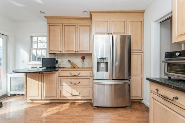 kitchen featuring light hardwood / wood-style floors, stainless steel fridge, light brown cabinetry, and dark stone counters