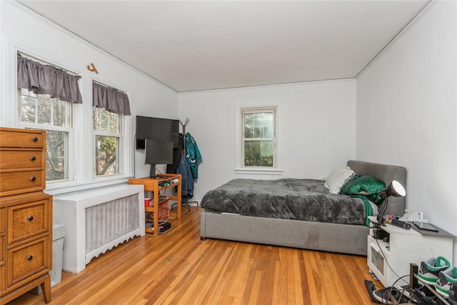 bedroom with radiator heating unit, multiple windows, and light wood-type flooring