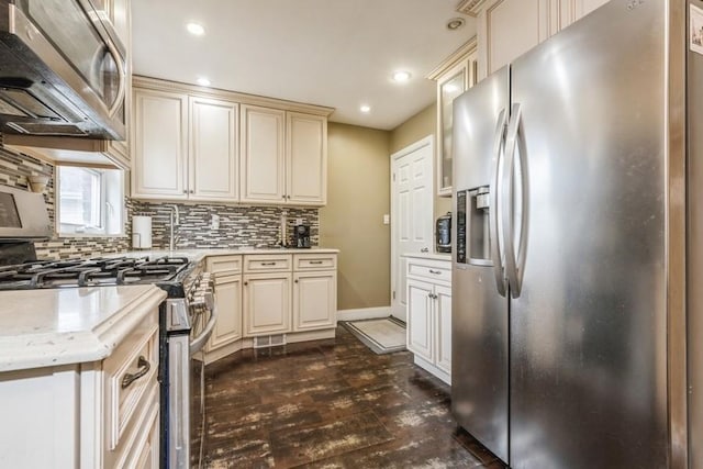 kitchen with dark wood-type flooring, stainless steel appliances, tasteful backsplash, cream cabinets, and light stone countertops