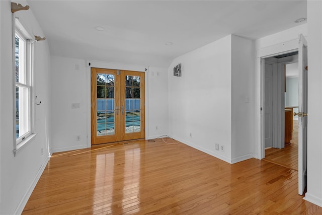 empty room with a wealth of natural light, french doors, and light wood-type flooring