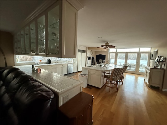 kitchen with light hardwood / wood-style floors, white cabinets, tile countertops, stainless steel dishwasher, and kitchen peninsula