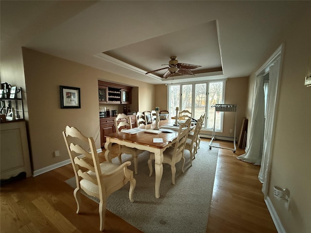 dining room featuring light hardwood / wood-style flooring, a raised ceiling, and ceiling fan