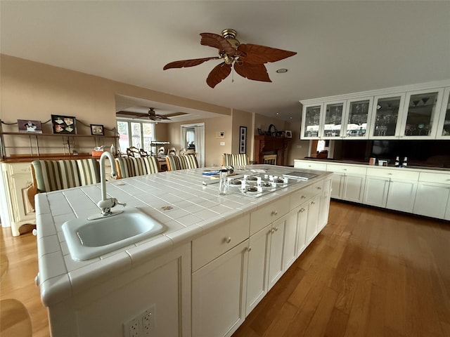 kitchen with sink, dark wood-type flooring, stainless steel gas cooktop, white cabinets, and tile countertops