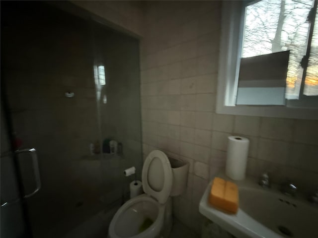 bathroom with toilet, a shower with shower door, sink, and tile walls