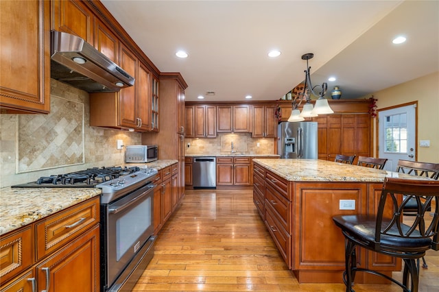 kitchen featuring appliances with stainless steel finishes, a kitchen island, a breakfast bar area, hanging light fixtures, and light stone countertops