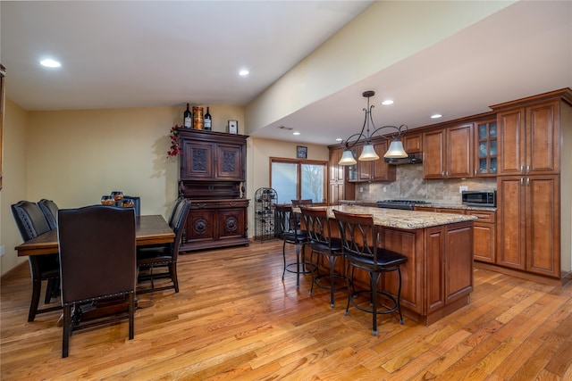 kitchen with decorative light fixtures, a center island, light wood-type flooring, light stone countertops, and decorative backsplash