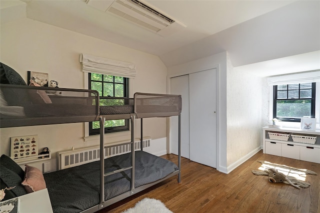 bedroom featuring hardwood / wood-style flooring, vaulted ceiling, radiator, and a closet