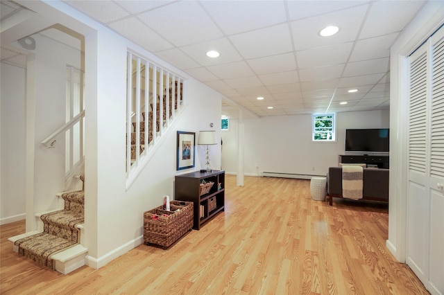 interior space with a baseboard heating unit, a drop ceiling, and light hardwood / wood-style flooring