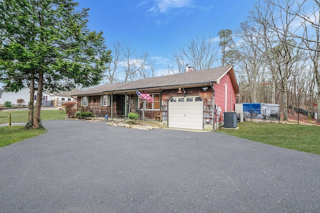 ranch-style home with aphalt driveway, an attached garage, fence, central AC, and a front yard