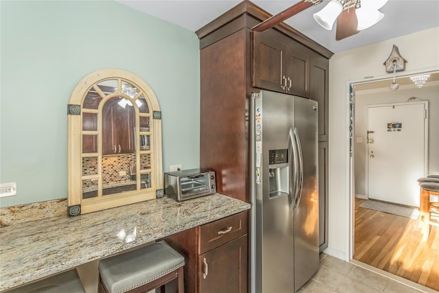 kitchen featuring stainless steel refrigerator with ice dispenser, dark brown cabinetry, light stone counters, and light tile patterned floors