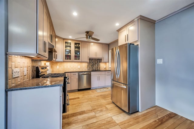 kitchen featuring ceiling fan, appliances with stainless steel finishes, dark stone countertops, light hardwood / wood-style floors, and decorative backsplash