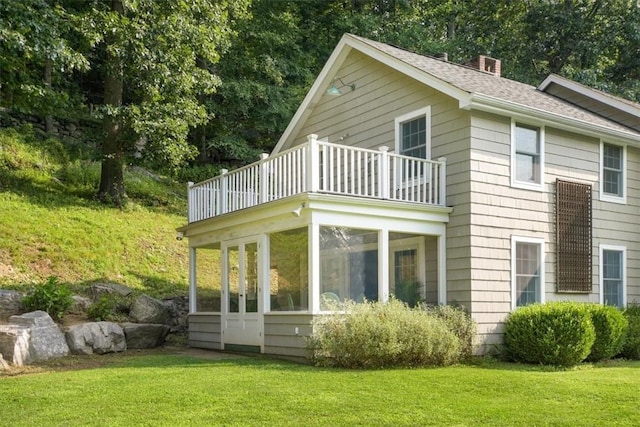 view of side of property featuring a balcony, a sunroom, and a lawn