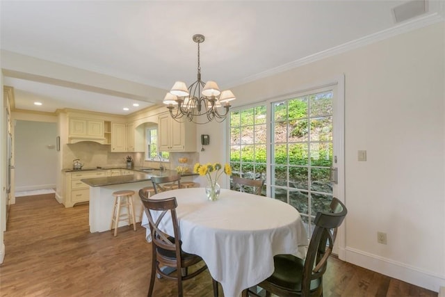 dining space with ornamental molding, dark wood-type flooring, sink, and an inviting chandelier