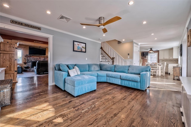 living room featuring crown molding, a stone fireplace, ceiling fan, and light wood-type flooring