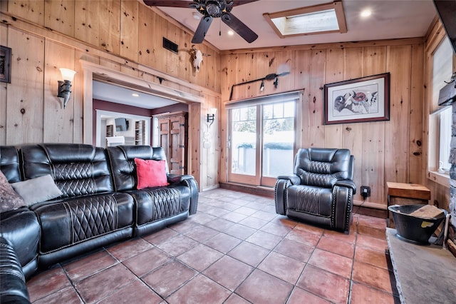 tiled living room with a skylight, wooden walls, and ceiling fan