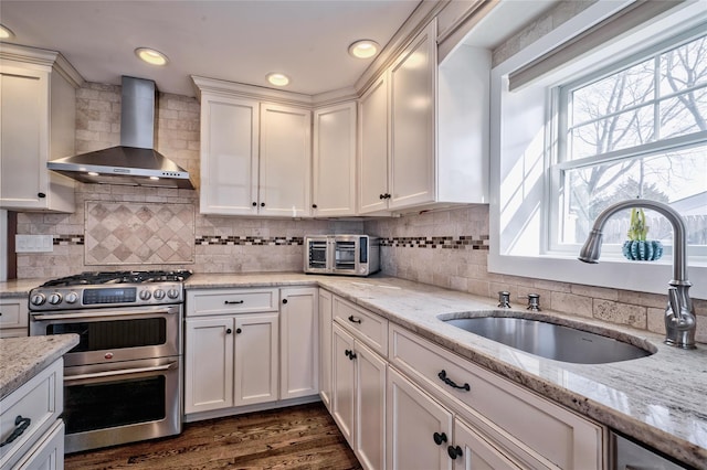 kitchen with sink, white cabinets, double oven range, light stone counters, and wall chimney exhaust hood