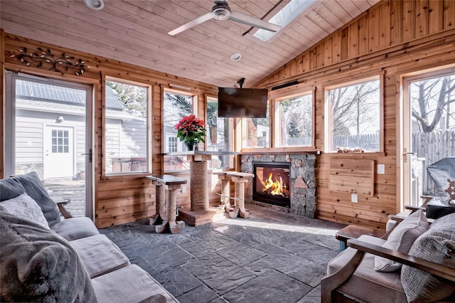 sunroom featuring wood ceiling, a fireplace, lofted ceiling with skylight, and ceiling fan