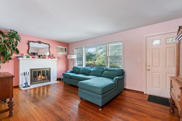 living room with a wall unit AC, dark hardwood / wood-style floors, and a brick fireplace