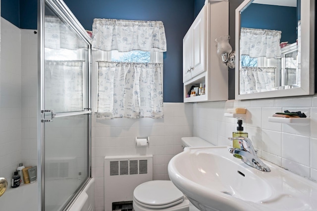 full bathroom with combined bath / shower with glass door, radiator, tile walls, and toilet