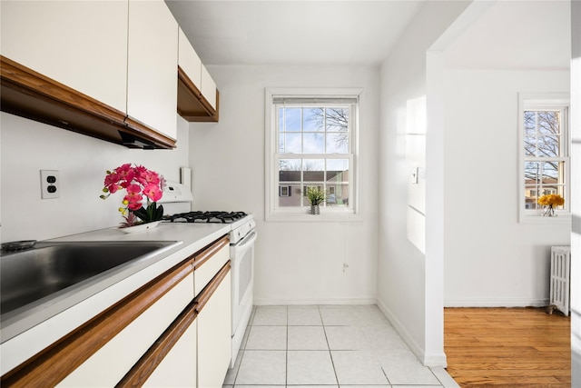 kitchen featuring white cabinetry, radiator, white gas range oven, and light tile patterned flooring