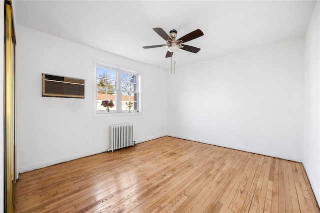 spare room featuring ceiling fan, a wall mounted air conditioner, radiator, and light wood-type flooring